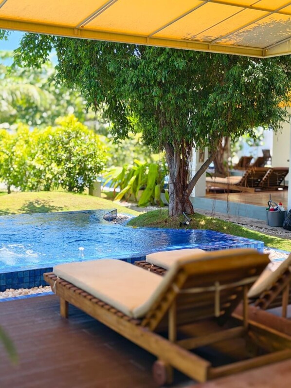 A pool area with lounge chairs, a tree, and a covered seating area. - Uppuveli Beach by DSK (Trincomalee)