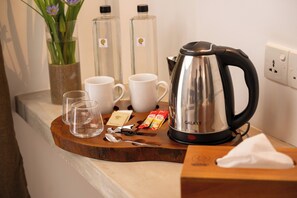 A kitchen counter with a coffee maker, two cups, a glass, a spoon, a napkin, and a box.