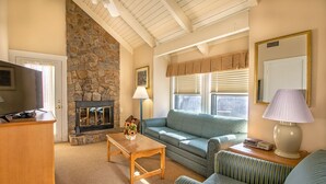 Una sala de estar acogedora con chimenea de piedra, televisor, sofá, mesa de centro y sillones a rayas.