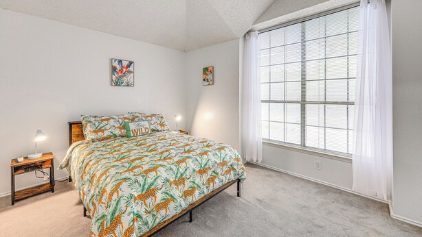 A bedroom with a large bed, a nightstand with a lamp, and a window with blinds. - Spacious San Antonio Home: Google Fiber, Game Room (San Antonio)