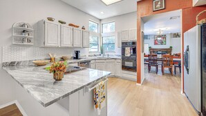 A modern kitchen with white cabinets, a marble countertop, and a dining area with wooden chairs. - Spacious San Antonio Home: Google Fiber, Game Room (San Antonio)