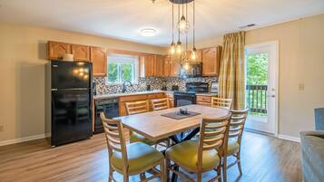 A modern kitchen with wooden cabinets, a black refrigerator, a dining table with chairs, and a hanging light fixture.