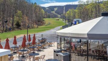 A terrace with outdoor seating, overlooking a forested valley and a ski slope.