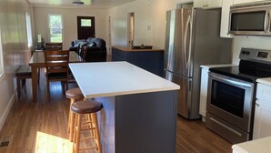 A modern kitchen with a central island, stainless steel appliances, and wooden flooring. - Riverview Retreat - house with sauna in the New River Gorge National Park! (Meadow Creek)