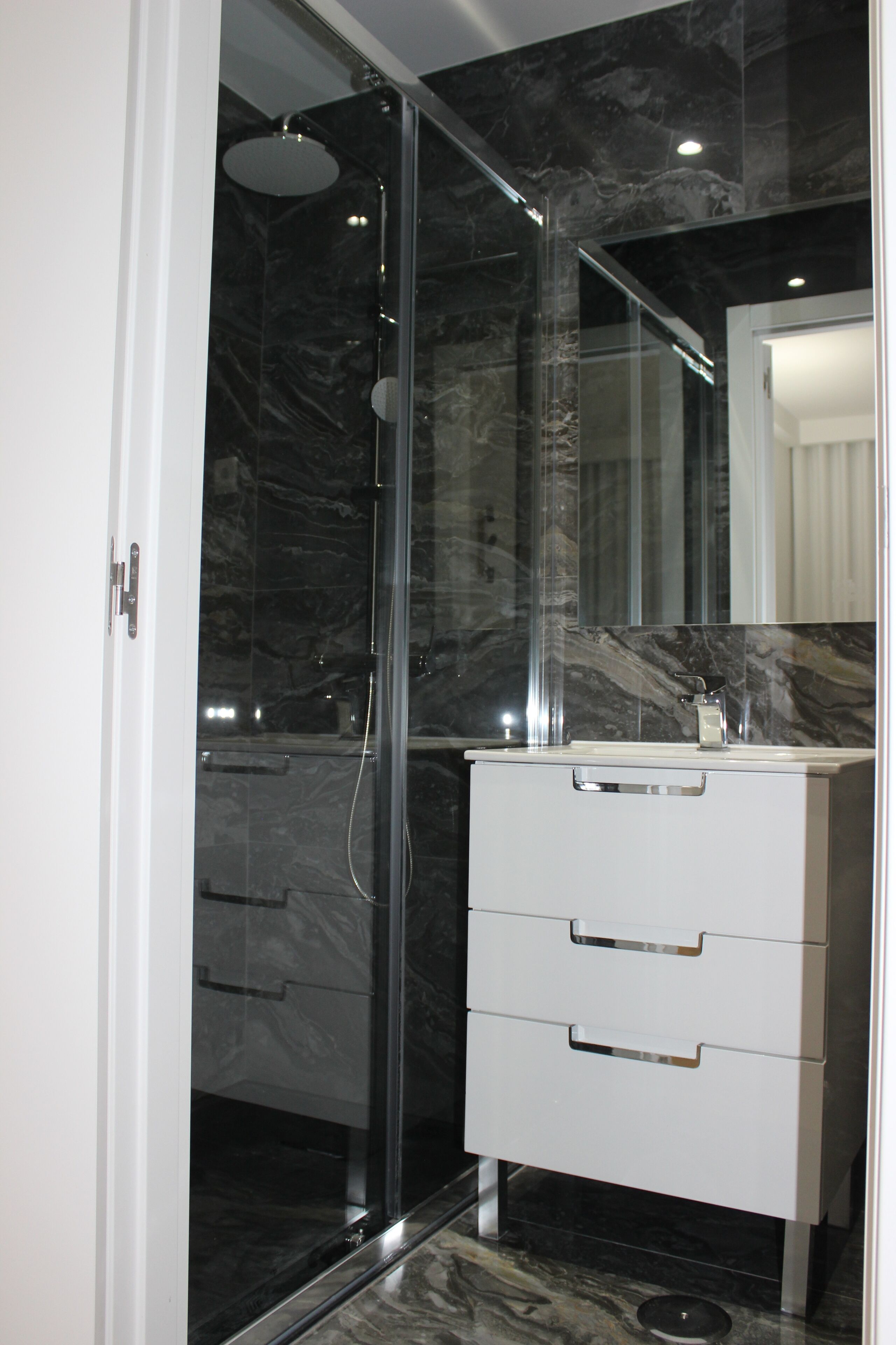 Une salle de bain moderne avec une douche à parois de verre, des murs en marbre et un meuble-lavabo blanc doté de tiroirs.