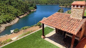 Una villa con una torre de piedra, techo de tejas y vista a un lago rodeado de bosque.