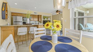 A modern kitchen with a central island, wooden cabinets, and a dining area with a round table and blue placemats. - Haven Harbor Getaway (Melbourne)