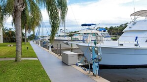 A marina with several boats docked, a grassy walkway, and palm trees. - Haven Harbor Getaway (Melbourne)