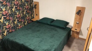 A bed with a green bedspread and pillows, flanked by wooden nightstands with lamps, in a room with a floral wallpaper.