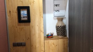A wooden door with a framed picture, a small shelf with a woven vase and a colorful bowl, and a wall-mounted electrical panel.
