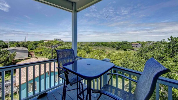 Un balcon avec une table et des chaises, donnant sur un paysage verdoyant et luxuriant ainsi que sur des maisons.