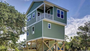 Une maison à deux étages avec un balcon à l’étage supérieur, entourée d’arbres.