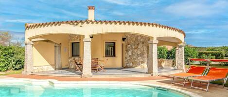 A villa with a swimming pool, outdoor seating, and a stone facade.