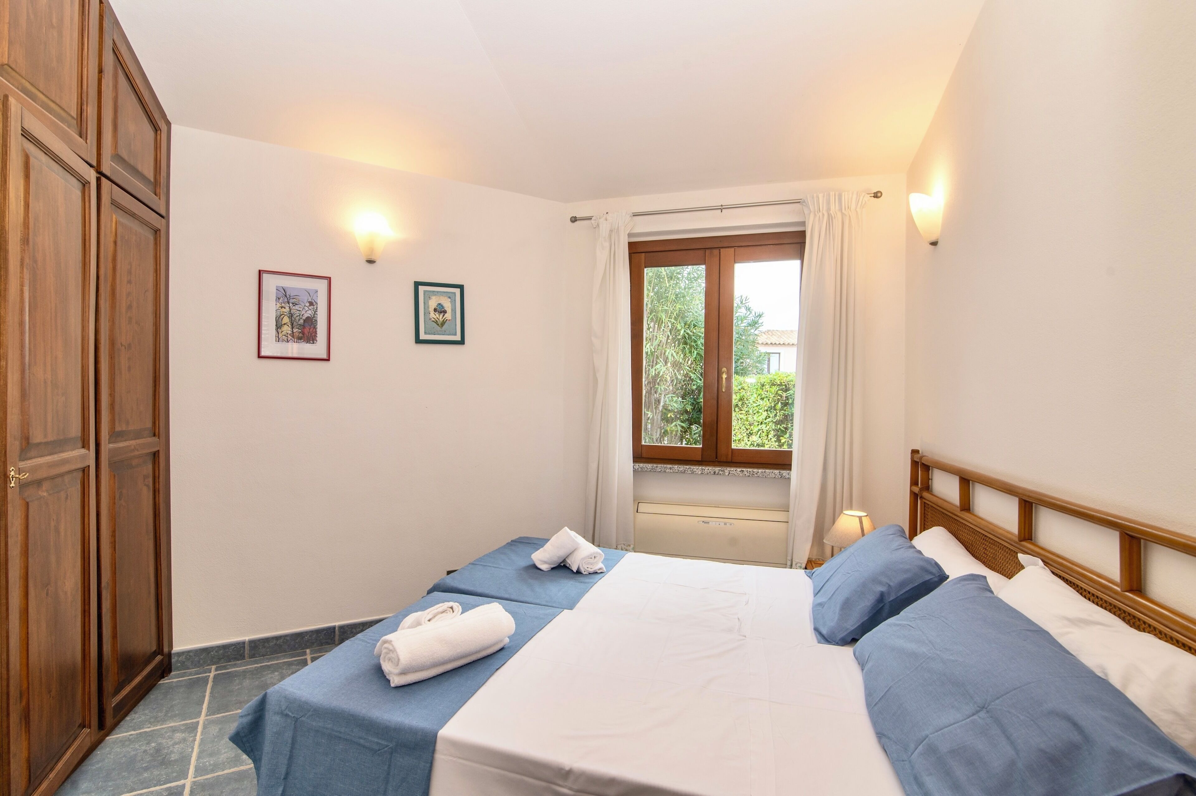 Camera d'albergo con due letti, una finestra con tende, un armadio in legno e luci a parete.