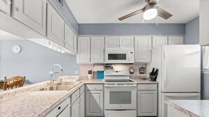 Una cocina con armarios blancos, microondas, estufa y refrigerador.