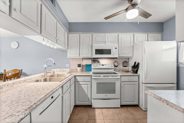 Una cocina con armarios blancos, microondas, estufa y refrigerador.