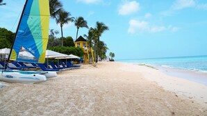 Une plage avec des chaises longues, un voilier et un bâtiment jaune.