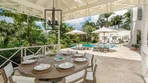 Un espace extérieur abrité, aménagé pour les repas, avec une piscine et des chaises longues en arrière-plan.