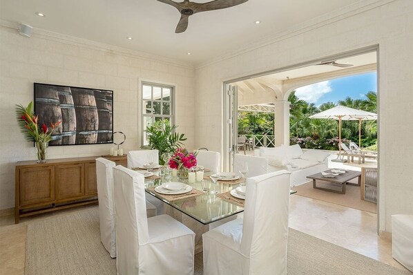 A spacious dining area with a glass table set for six, surrounded by white chairs. A wooden cabinet and a large painting adorn the walls. - One Westland Heights 5 Bedroom Villa (Westmoreland)