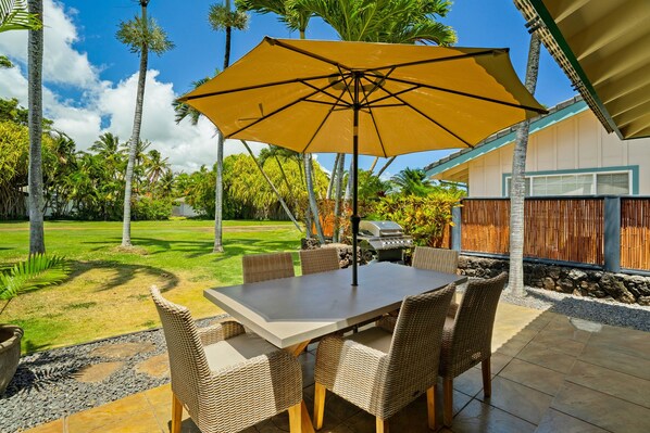 Un patio al aire libre con una mesa, sillas, una sombrilla grande y una parrilla.