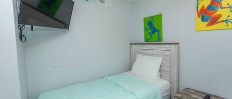 A small, neatly arranged bedroom with a bed, a TV mounted on the wall, and two paintings on the wall.