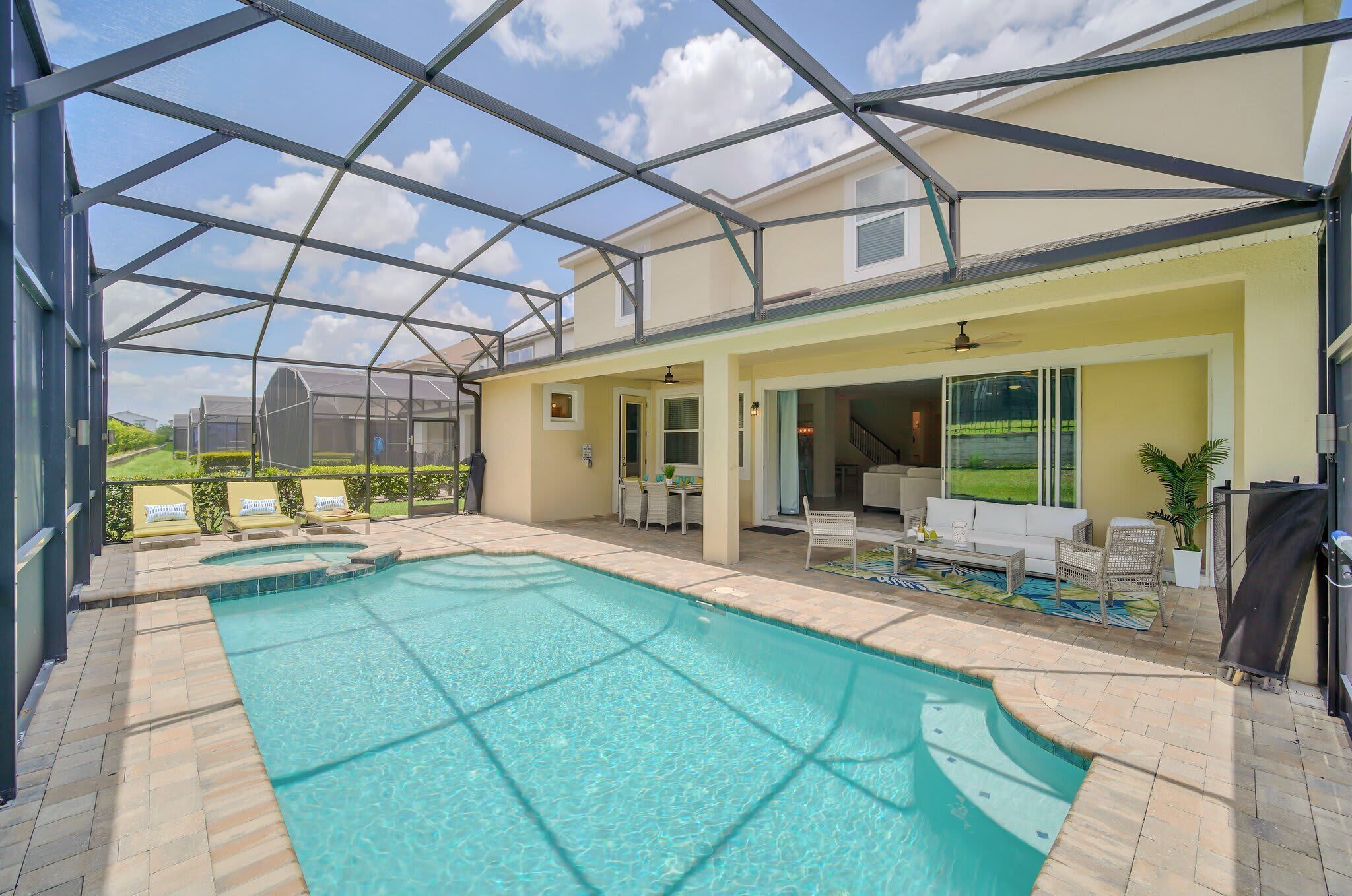 A covered outdoor swimming pool with a glass ceiling, a patio area with seating, and a view of a green landscape.