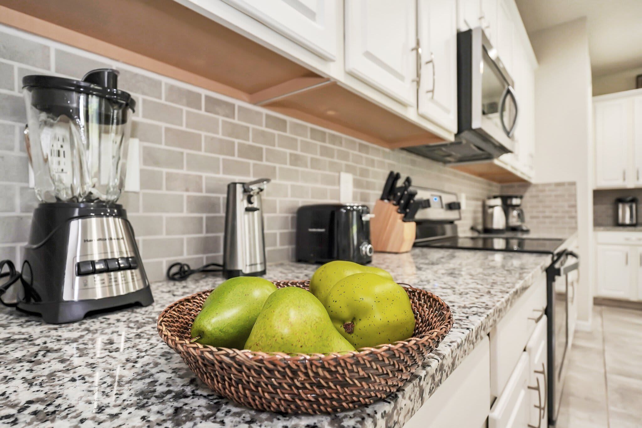 A kitchen with a granite countertop, a blender, a toaster, and a basket of green apples.
