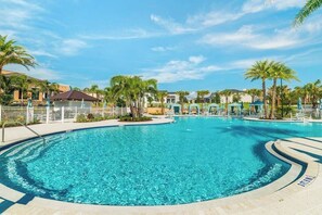 A large, clear swimming pool with a curved edge, surrounded by palm trees and a fence. - Elegant Family Home w/ Pool, Game Room, Themed Bedrooms (Kissimmee)