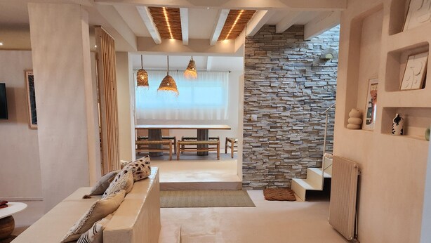 A modern living room with a sofa, dining area, and stone wall.