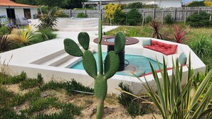 A pool area with a cactus centerpiece, surrounded by a wooden deck and a white wall.