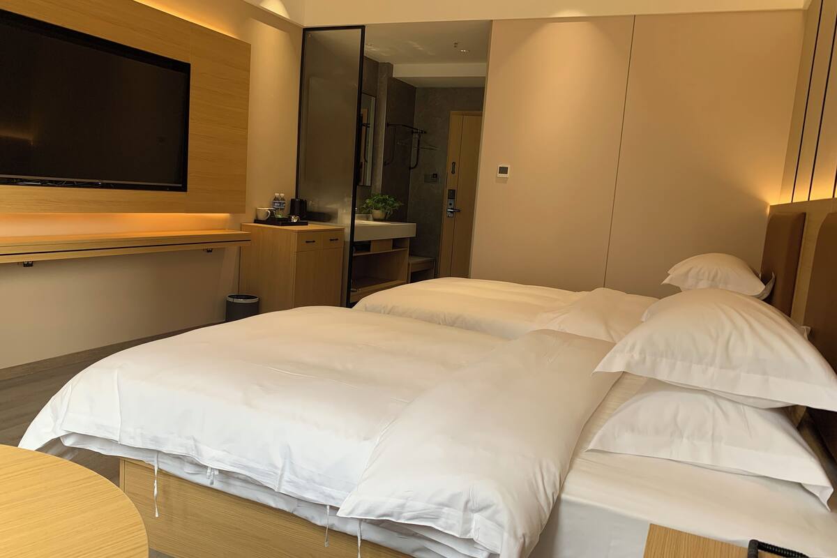 Una habitación de hotel moderna con una cama grande, un televisor de pantalla plana montado en la pared, un escritorio pequeño con una silla y un espejo.