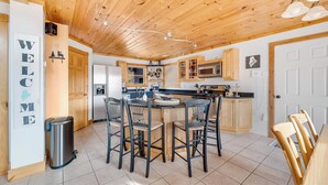 Een moderne keuken met houten kastjes, een centraal kookeiland met barstoelen en een roestvrijstalen koelkast.