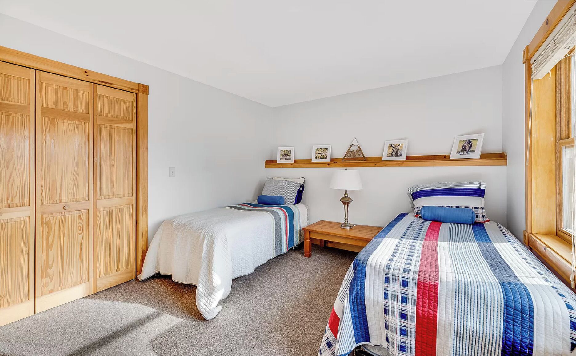 A bedroom with two beds, wooden wardrobe, and a shelf with photos.
