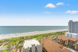 A coastal hotel with a view of the beach, a parking area, and a pool.