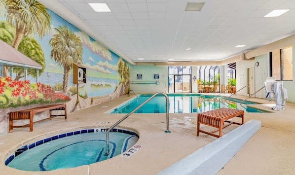 Ein Hallenbad mit Wandgemälde einer tropischen Szene, einem Rettungsschwimmerstuhl und einer Bank.