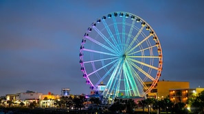 Ein großes Riesenrad mit bunten Lichtern, umgeben von Gebäuden und Palmen.