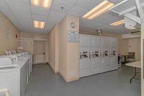 A laundry facility with multiple washing machines and dryers, a clock on the wall, and a notice sign.