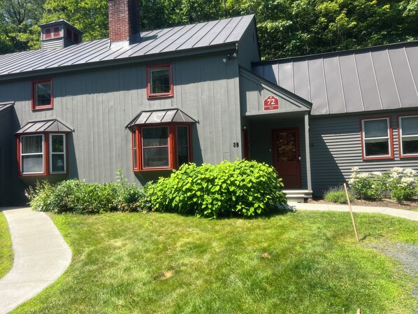 A two-story building with a gray exterior, red-framed windows, and a chimney.