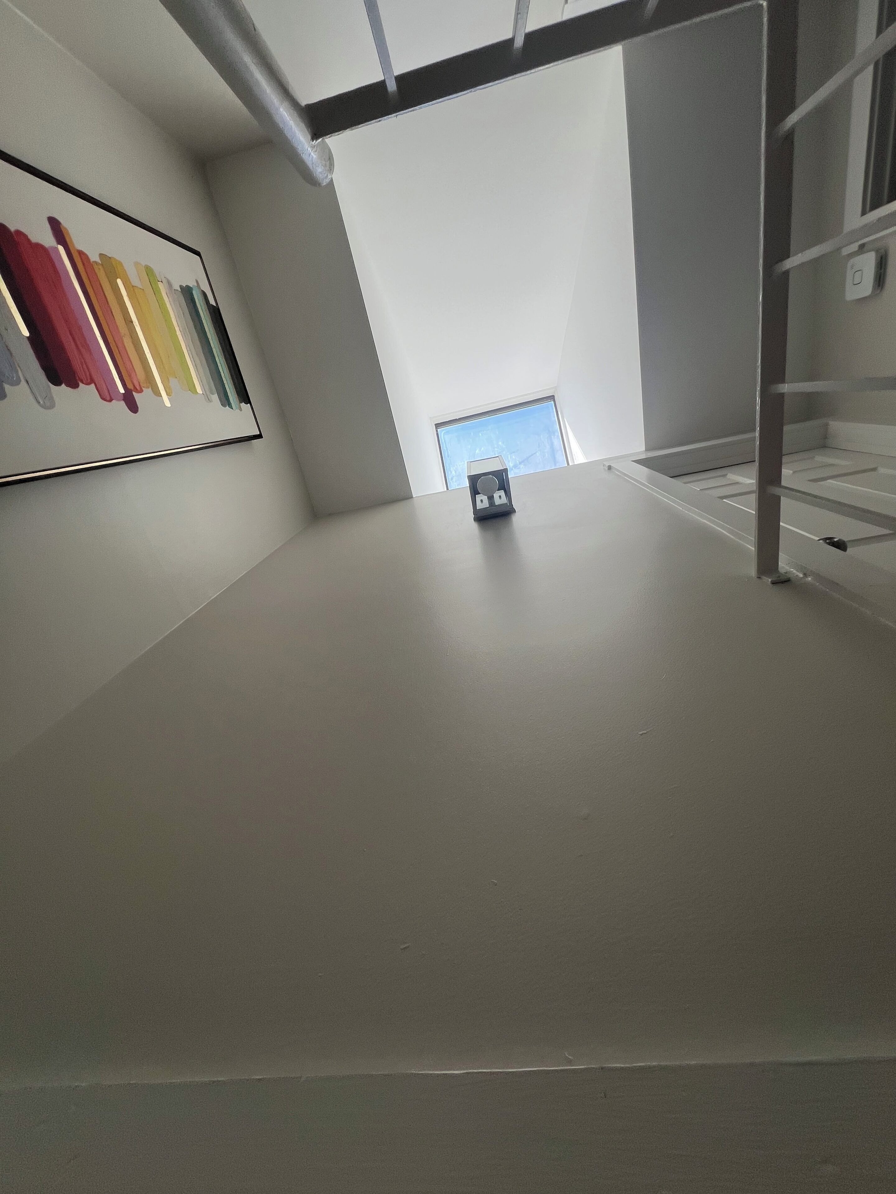 A room with a sloped ceiling, a framed artwork on the wall, and a small table with a box on it.