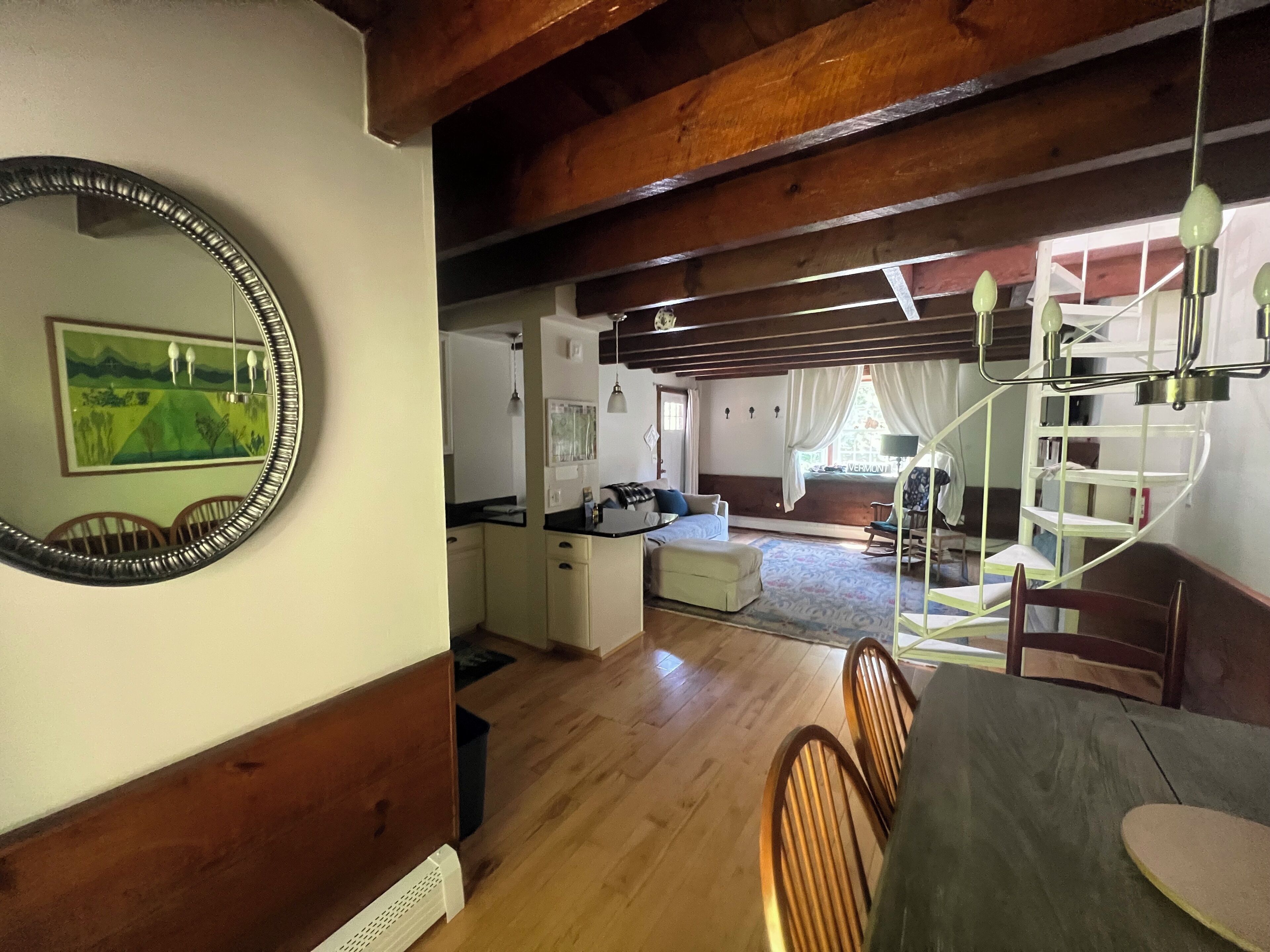 A room with a dining table, chairs, a mirror, a kitchen area, and a staircase.