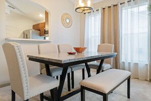 A dining area with a marble table, cushioned chairs, a bench, a decorative bowl, and a modern chandelier.