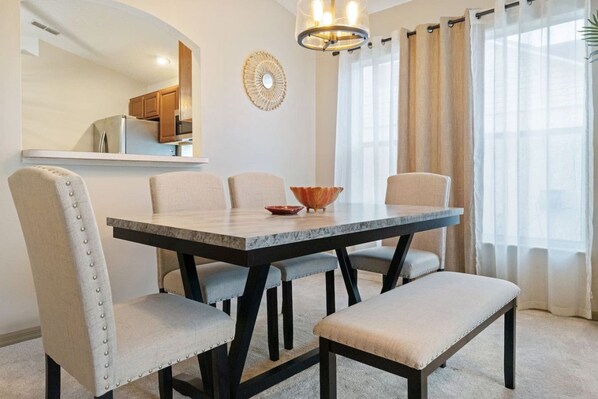 Un espace repas comprenant une table en marbre, des chaises rembourrées, un banc, un vase décoratif et un lustre moderne.