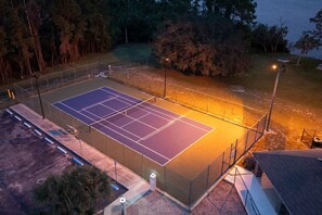 Ein Tennisplatz mit umgebender Umzäunung und einem Gebäude im Hintergrund.