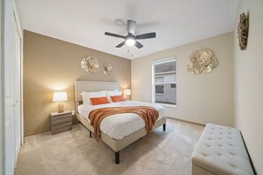 Ein Schlafzimmer mit Bett, Nachttisch, Lampe, Deckenventilator, Wanddekoration und einem Fenster.
