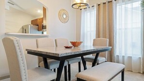 A dining area with a marble table, four upholstered chairs, and a decorative wall piece.