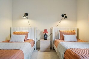 Une chambre double avec deux lits, chacun doté d’une tête de lit blanche et d’une literie orange. Deux lampes murales sont fixées de chaque côté des lits.