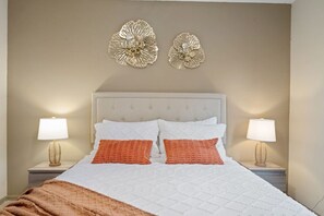 Una cama bien hecha con ropa de cama blanca y naranja, flanqueada por dos lámparas de noche sobre mesitas a juego.