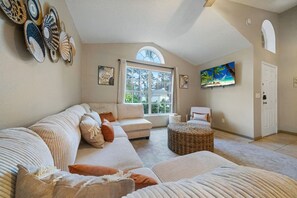 Ein geräumiges Wohnzimmer mit großem Fenster, einer Sofagarnitur, einem Fernseher und einer Tür.