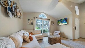 A spacious living room with a large window, a sofa, a chair, and a TV.