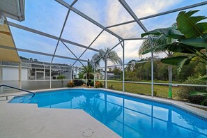 Una piscina con vistas claras del paisaje circundante, incluyendo palmeras y una casa.